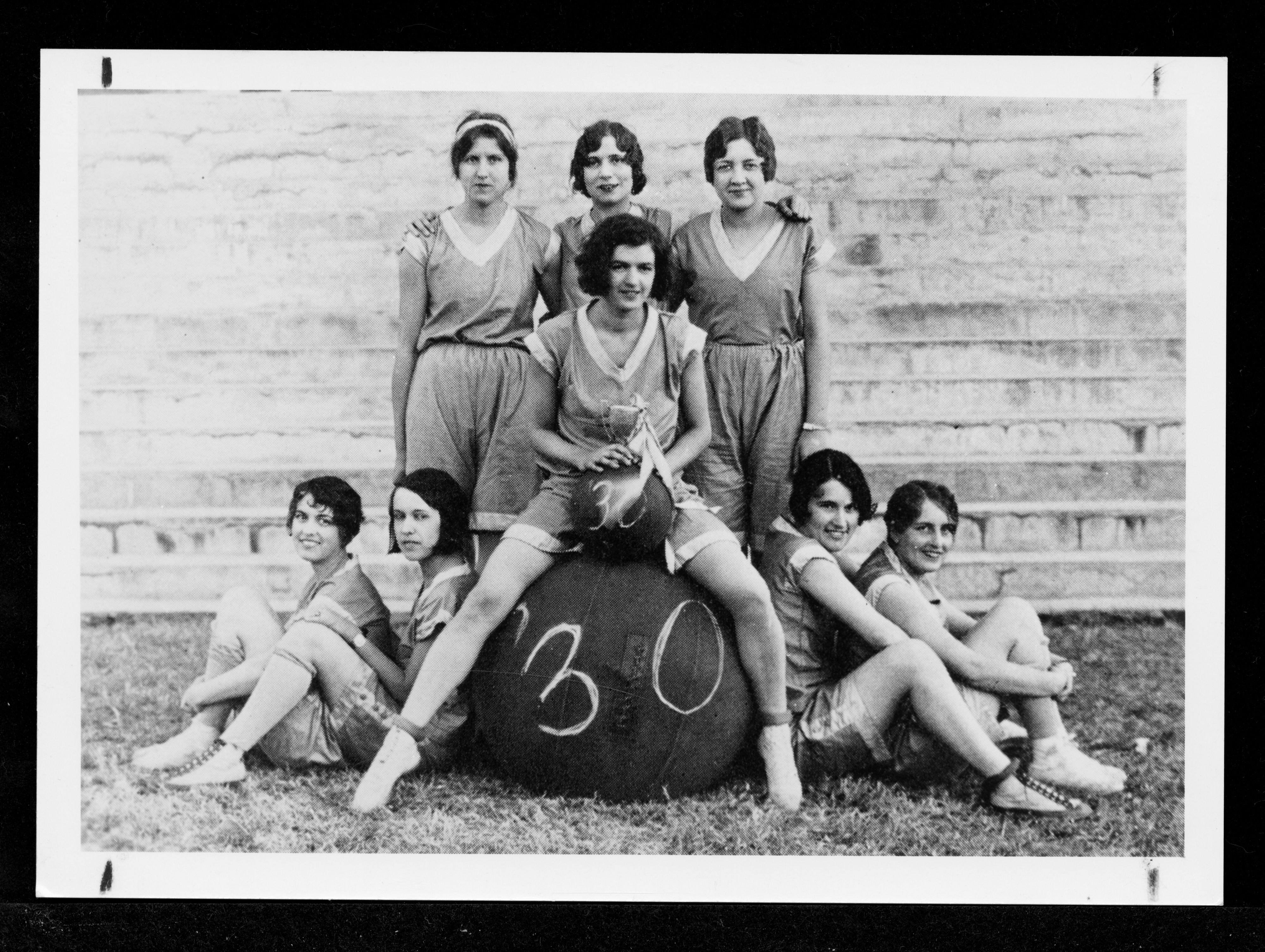 Women sitting on and around a large ball with the number 30 on it.