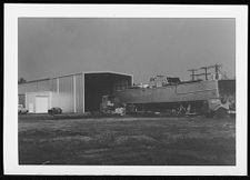 Osprey:  Portside view of boat on land coming out of warehouse.