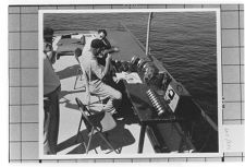 Speed Boats.  Three men sitting and a desk on dock