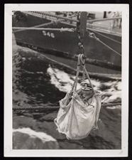 Man in canvas bag over water between ships 