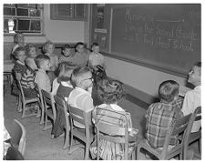 Children Sitting in a Circle of Chairs Facing the Blackboard