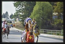 Photograph of man in Native American headdress riding a horse.