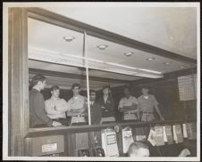 Photograph of Air Force ROTC Cadets and other people standing behind a glass divider