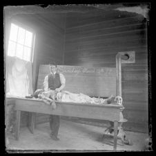 Man standing over a dead body laid out on a table